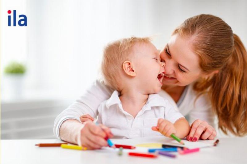 Một đứa trẻ nhỏ đang ngồi tập trung tô màu trên giấy với bút màu sáp, thể hiện sự phối hợp tay mắt và kỹ năng vận động tinh